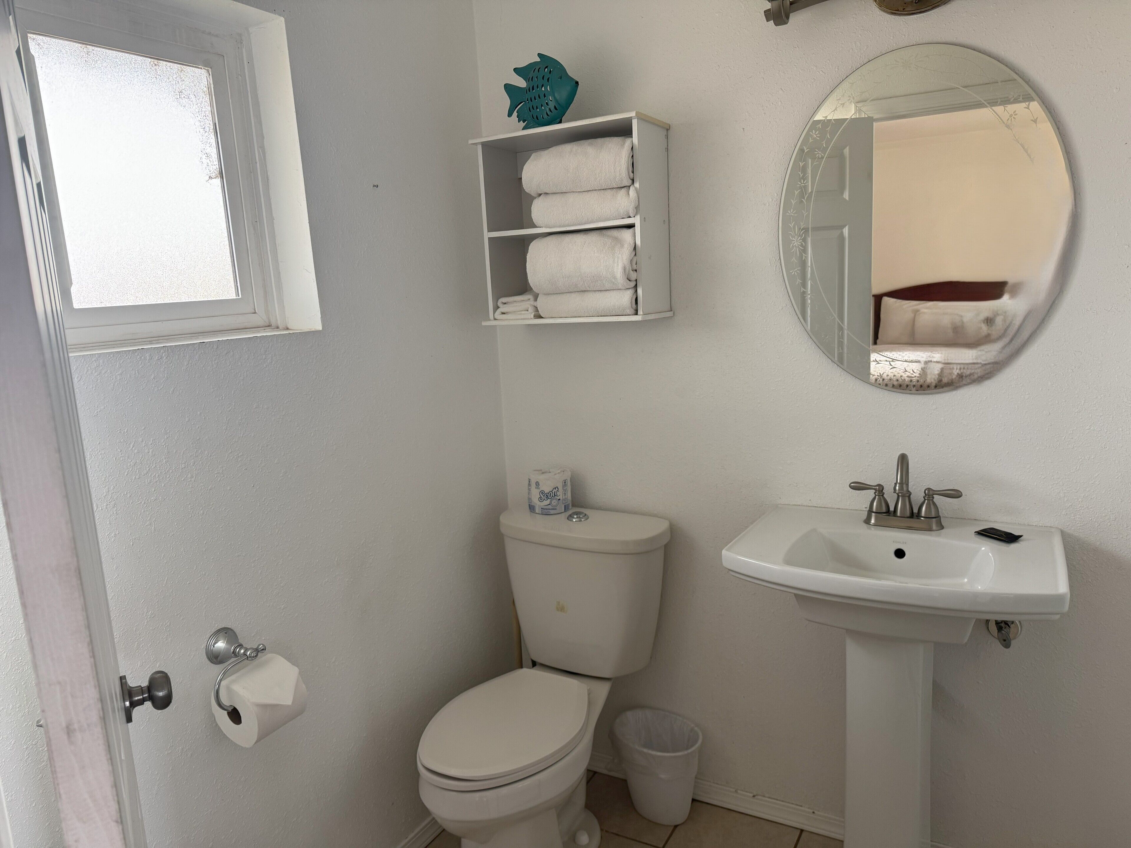 A bathroom with a toilet, sink, and a shelf with towels.