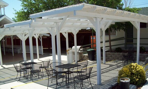 A covered outdoor seating area with tables and chairs, a grill, and a trash can. - Lakeshore Lodge (Wofford Heights)