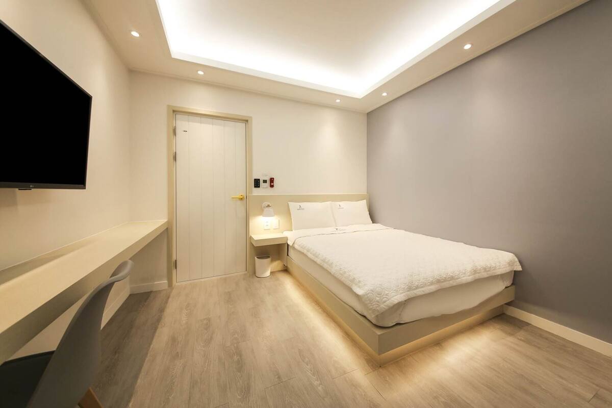 Une chambre d’hôtel moderne équipée d’un lit, d’une table de chevet et d’un téléviseur à écran plat fixé au mur.