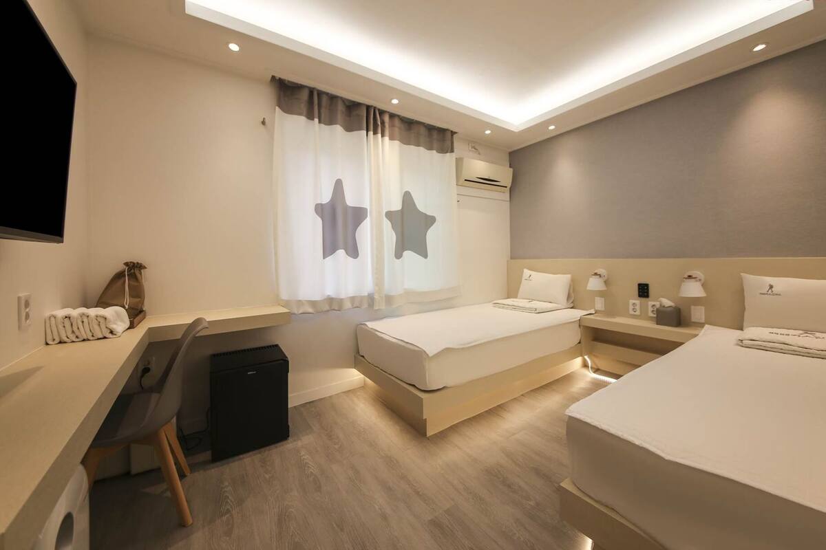 Une chambre d’hôtel moderne, équipée d’un lit, d’un bureau et d’une chaise, ainsi que d’une petite valise noire et d’un rideau en forme d’étoile.