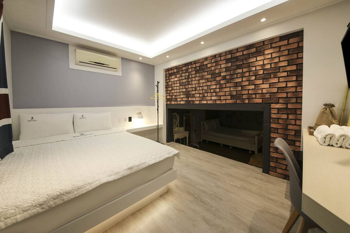 Une chambre à coucher moderne avec un grand lit, une cheminée en briques et une lucarne au-dessus du lit.