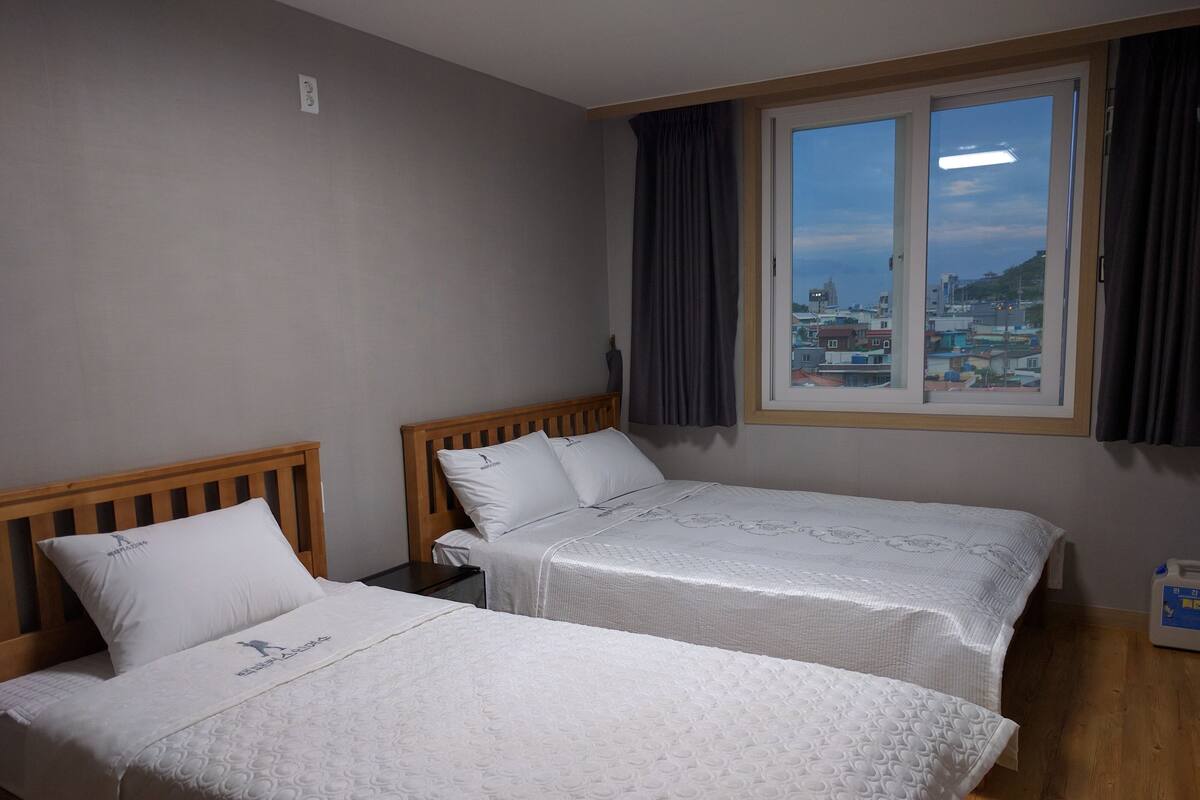 Une chambre d’hôtel avec deux lits simples, une fenêtre avec des rideaux et une vue sur les bâtiments environnants.