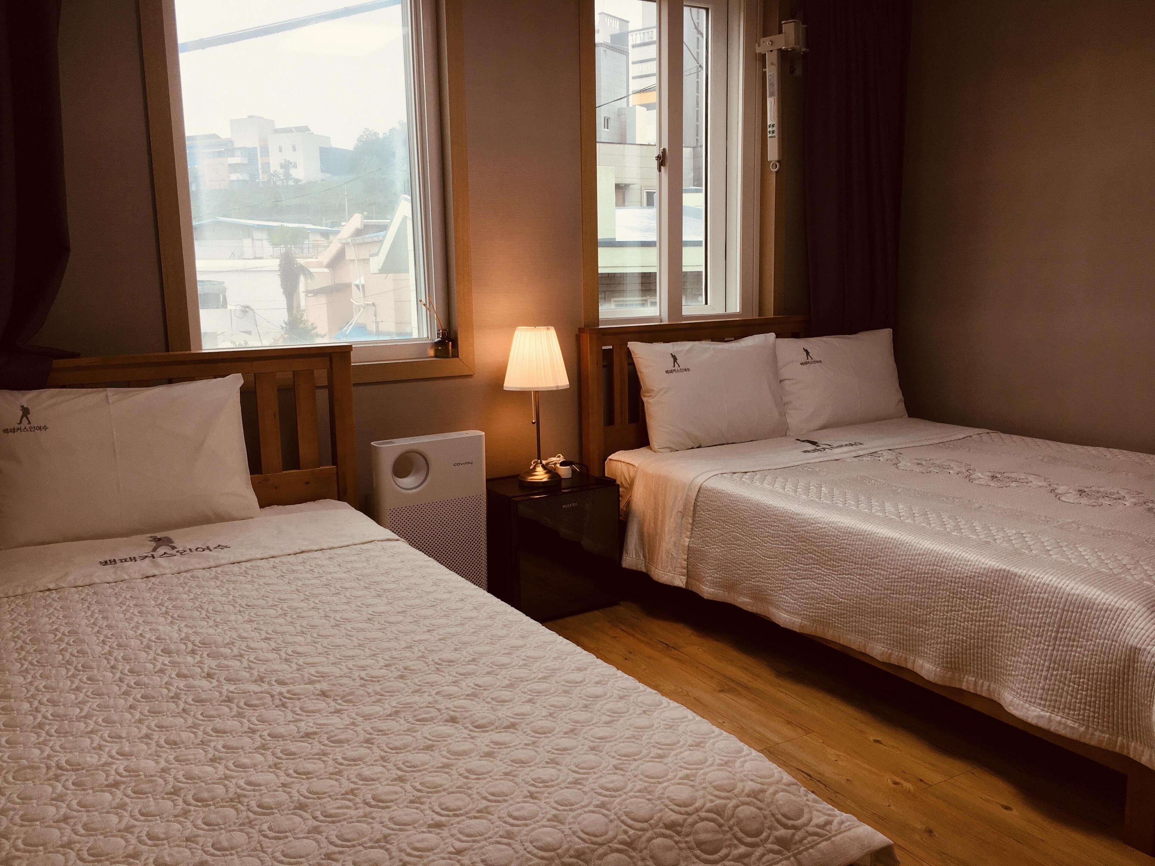 A hotel room with two beds, a window, a lamp, and a radiator.