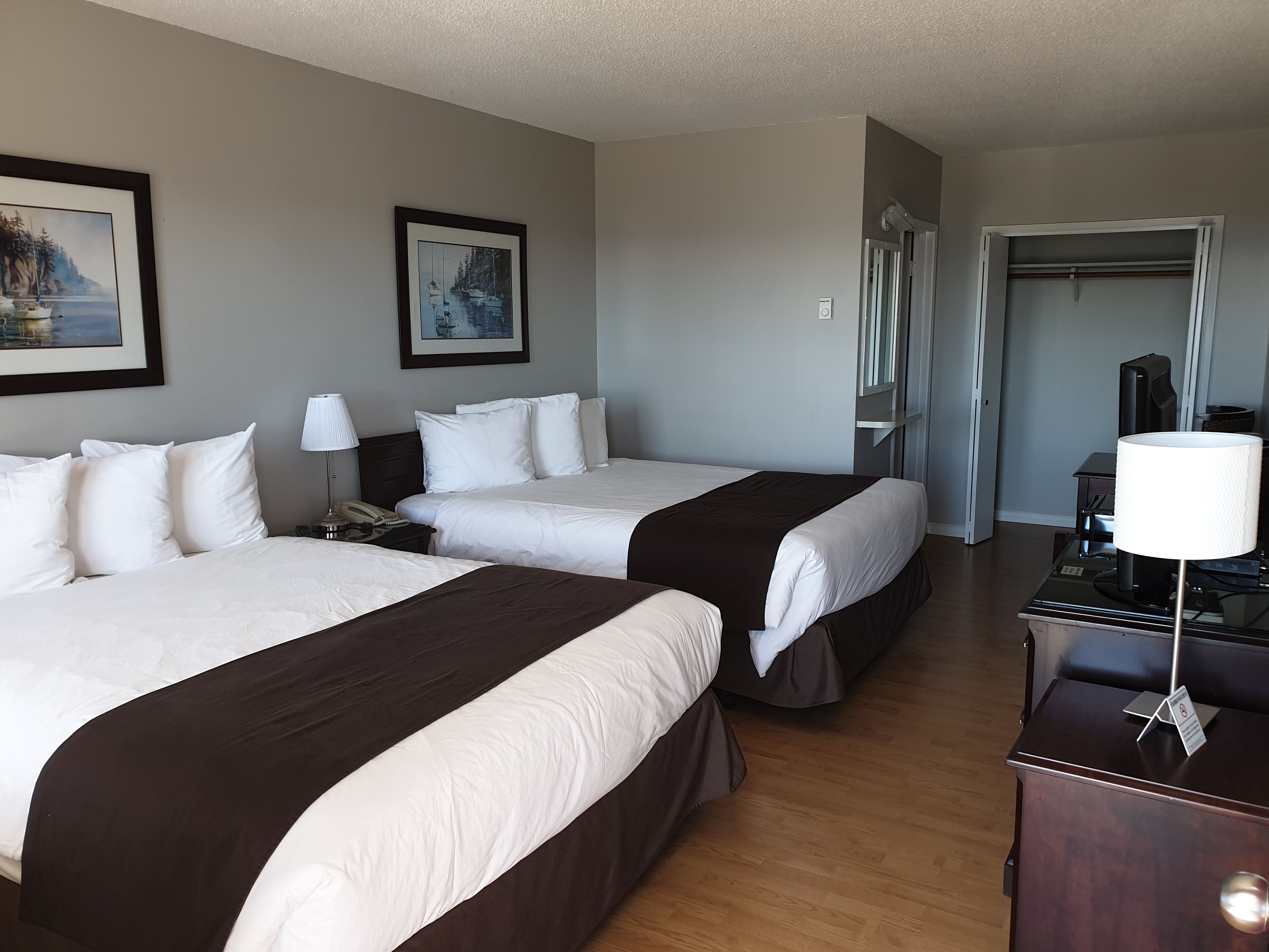 A hotel room with two beds, a desk, a lamp, and a painting on the wall.