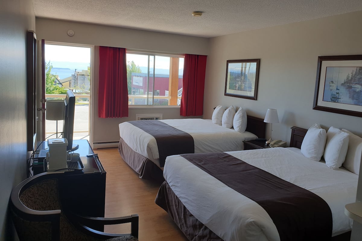 Habitación de hotel con dos camas, un escritorio con computadora, una silla y una ventana con cortinas rojas.