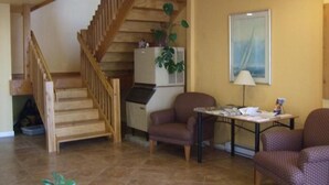 A living room with a wooden staircase, a dining table, two armchairs, a refrigerator, and a painting on the wall. - Island View Lodge (Powell River)