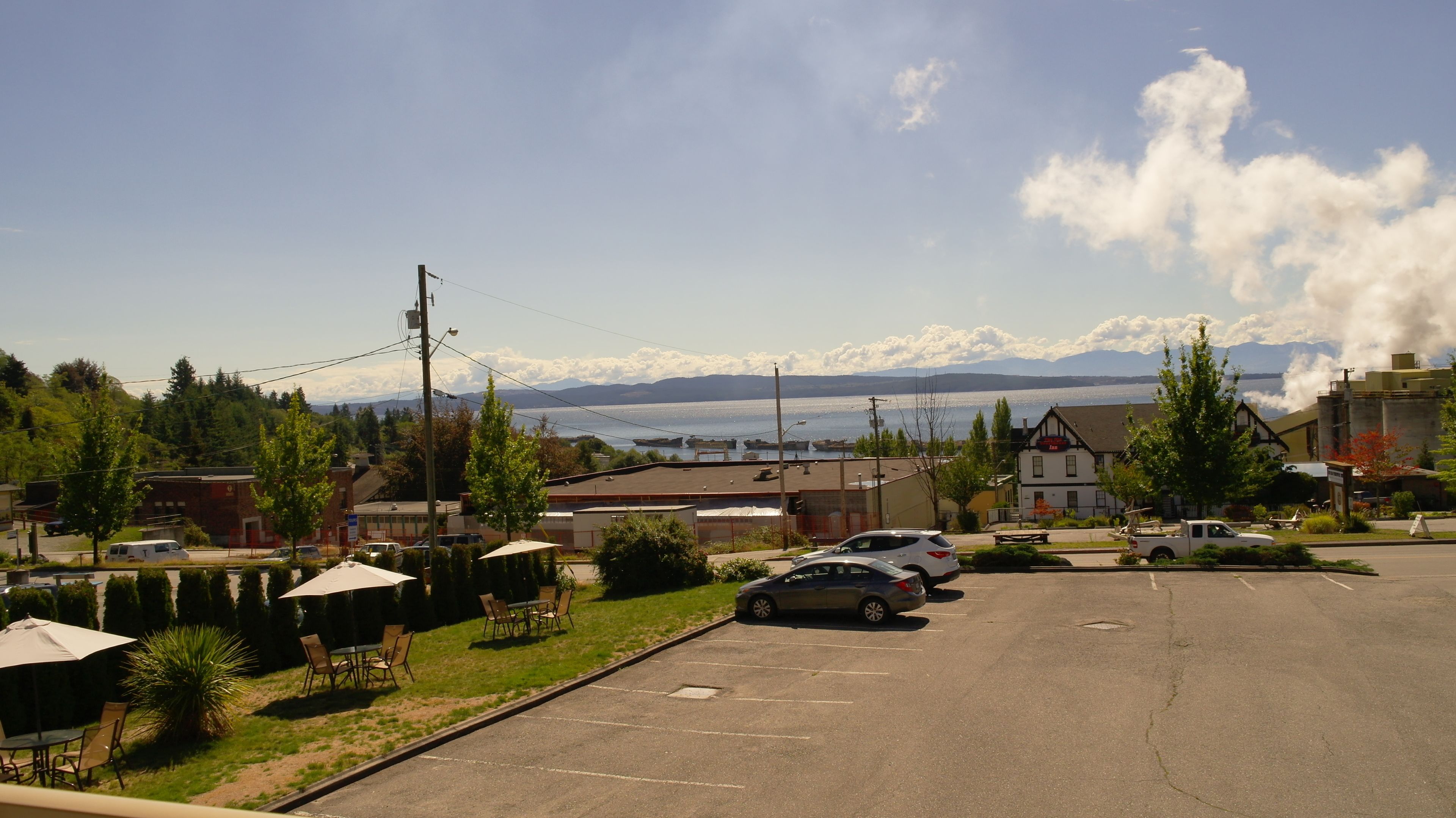 A parking lot with cars, a building with a sign, and a view of mountains and water.