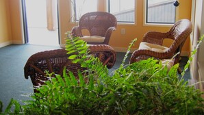 A room with two wicker chairs and a small table, large windows with blinds, and a lamp. - Island View Lodge (Powell River)