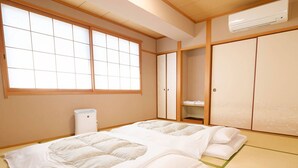 A traditional Japanese-style room with tatami flooring, a futon bed, sliding shoji doors, and a built-in air conditioning unit. - Tennen Onsen Matsuyama New Grand Hotel (Matsuyama)