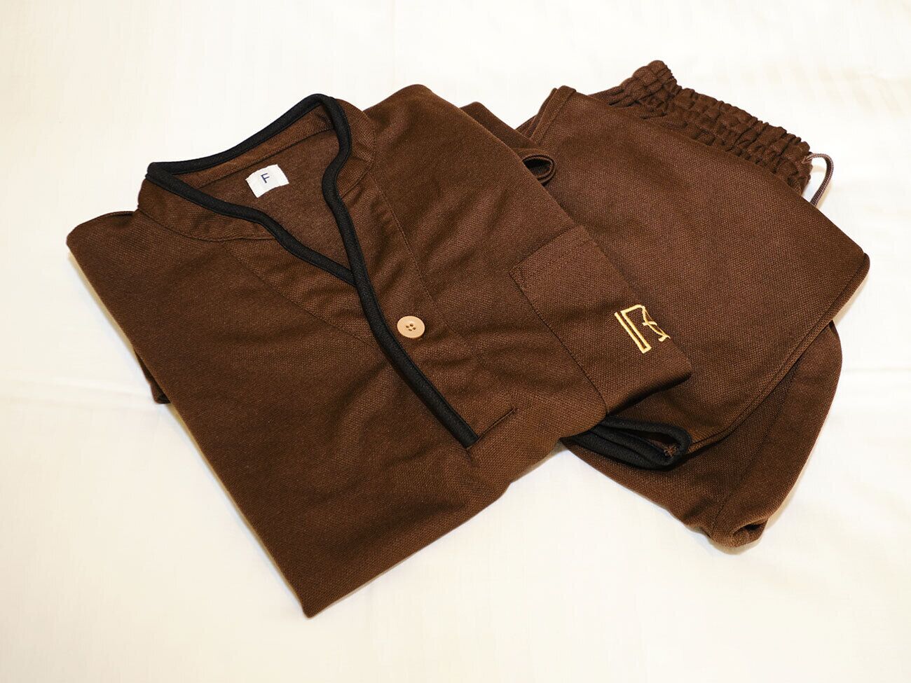 A pair of brown pants with a black drawstring and a small embroidered logo.