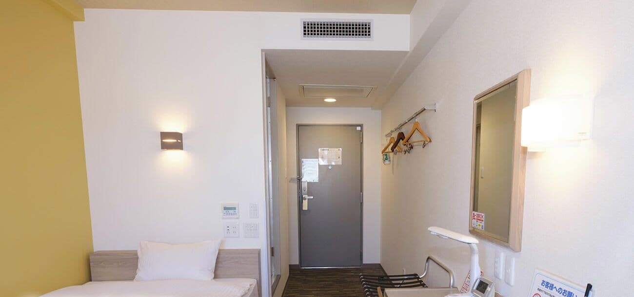 A hotel room with a bed, a desk, a chair, a mirror, and a door leading to another room.