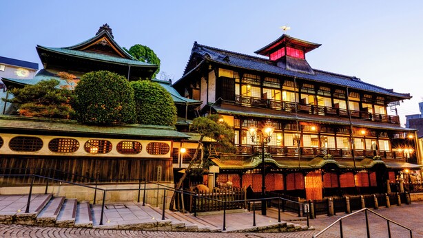 A traditional Japanese building with multiple stories, wooden railings, and a tiled roof. - Tennen Onsen Matsuyama New Grand Hotel (Matsuyama)