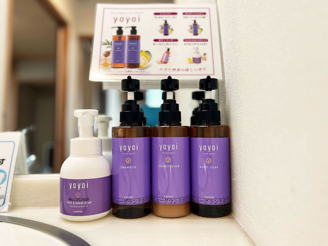 A bathroom shelf with three bottles of yayoï shampoo, conditioner, and body soap, and a white bottle of face & hand soap.