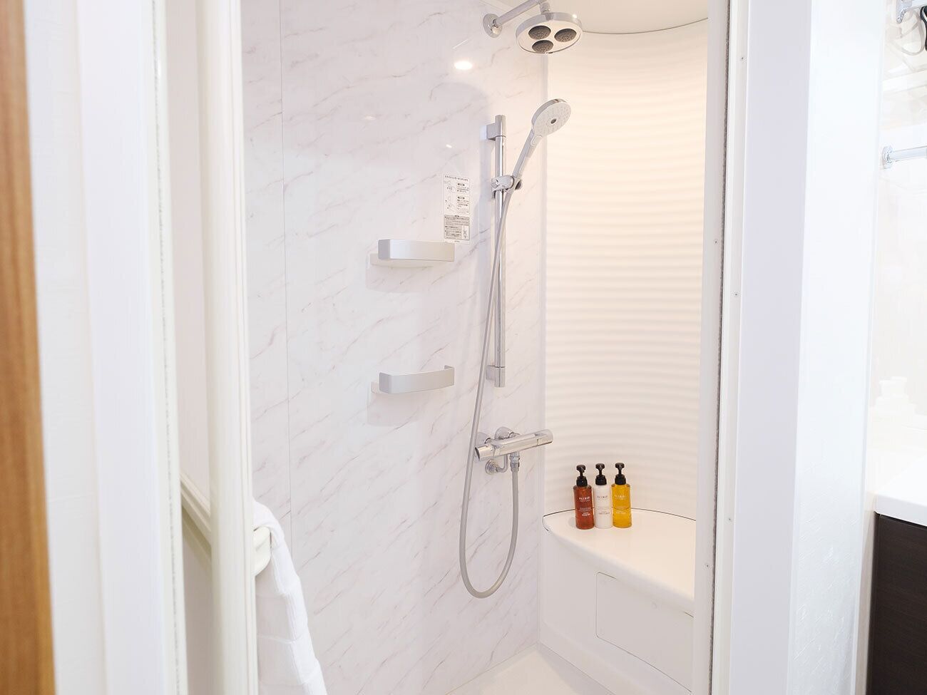 Un baño moderno con ducha, inodoro y un estante con artículos de aseo.