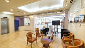 A hotel lobby with a reception desk, seating area, and a large TV screen. - Tennen Onsen Matsuyama New Grand Hotel (Matsuyama)