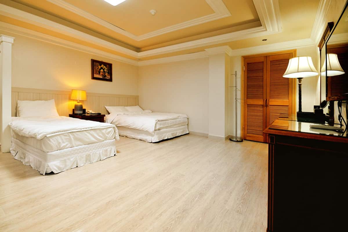 A hotel room with two beds, a nightstand with a lamp, a wooden wardrobe, and a mirror.