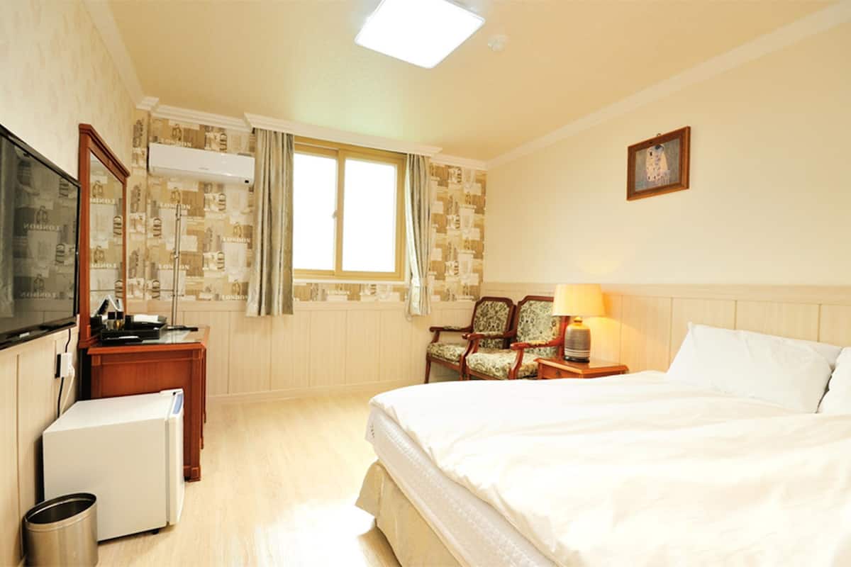A hotel room with a bed, a desk, a chair, a television, and a window with curtains.