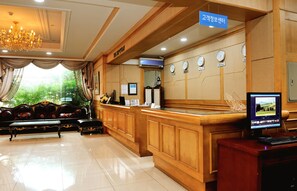A reception area with a wooden reception desk, a computer monitor, and a seating area with a sofa and a bench. - Chambord Hotel (Yeosu)