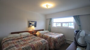 Une chambre d’hôtel avec deux lits, un bureau avec un ventilateur, une fenêtre avec des rideaux et une lampe sur la table de chevet.