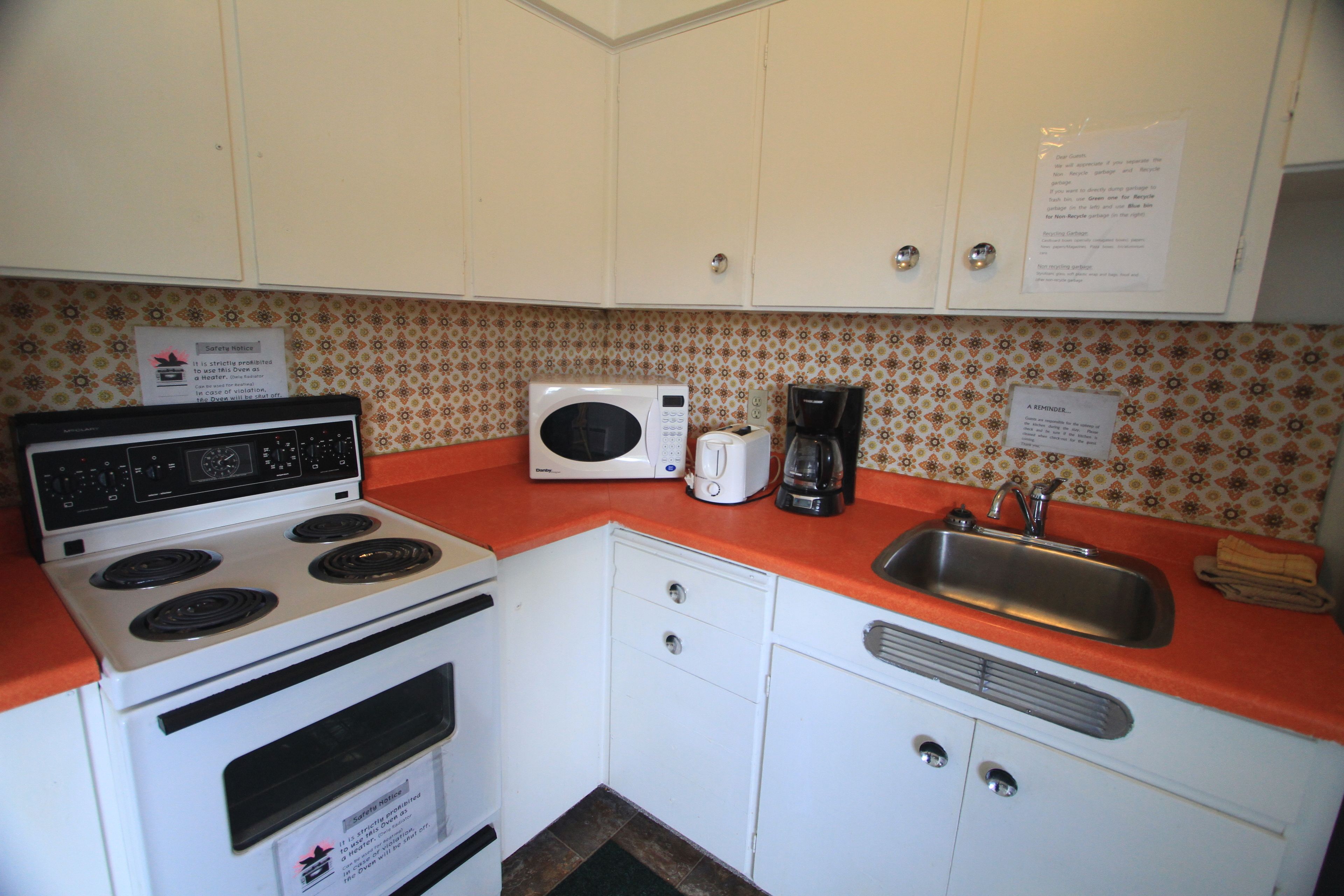 A compact kitchen with white cabinets, a stove, a microwave, and a sink.