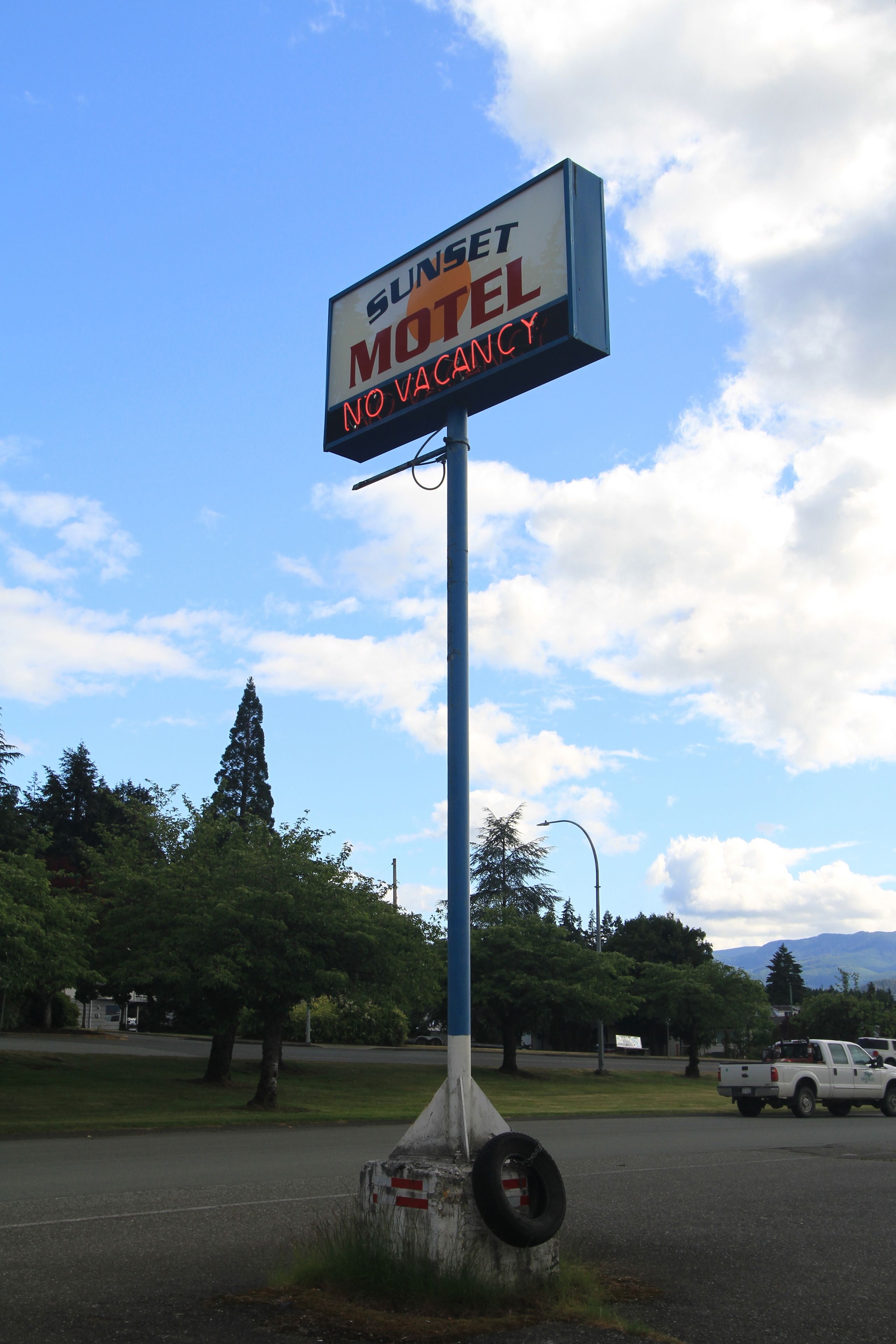 A motel sign with a blue pole and a tire at the base.