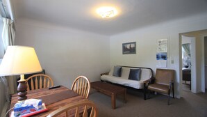 Une pièce comprenant une table à manger en bois, des chaises, un canapé, une table basse et une lampe. Une télécommande se trouve sur la table.