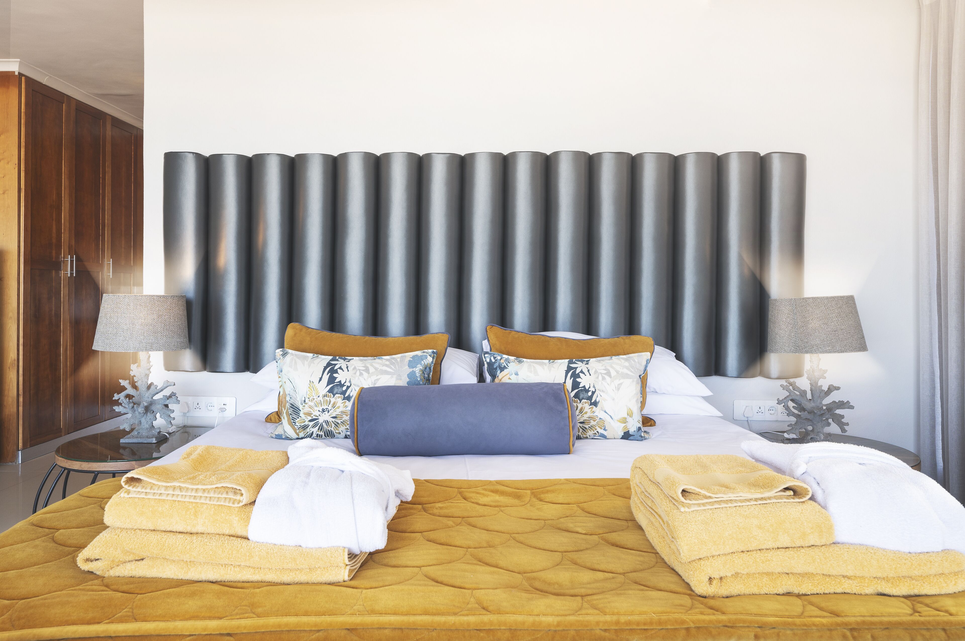 Una habitación de hotel con una cama grande, dos lámparas de noche, un cabecero y una mesita de noche con un objeto decorativo.