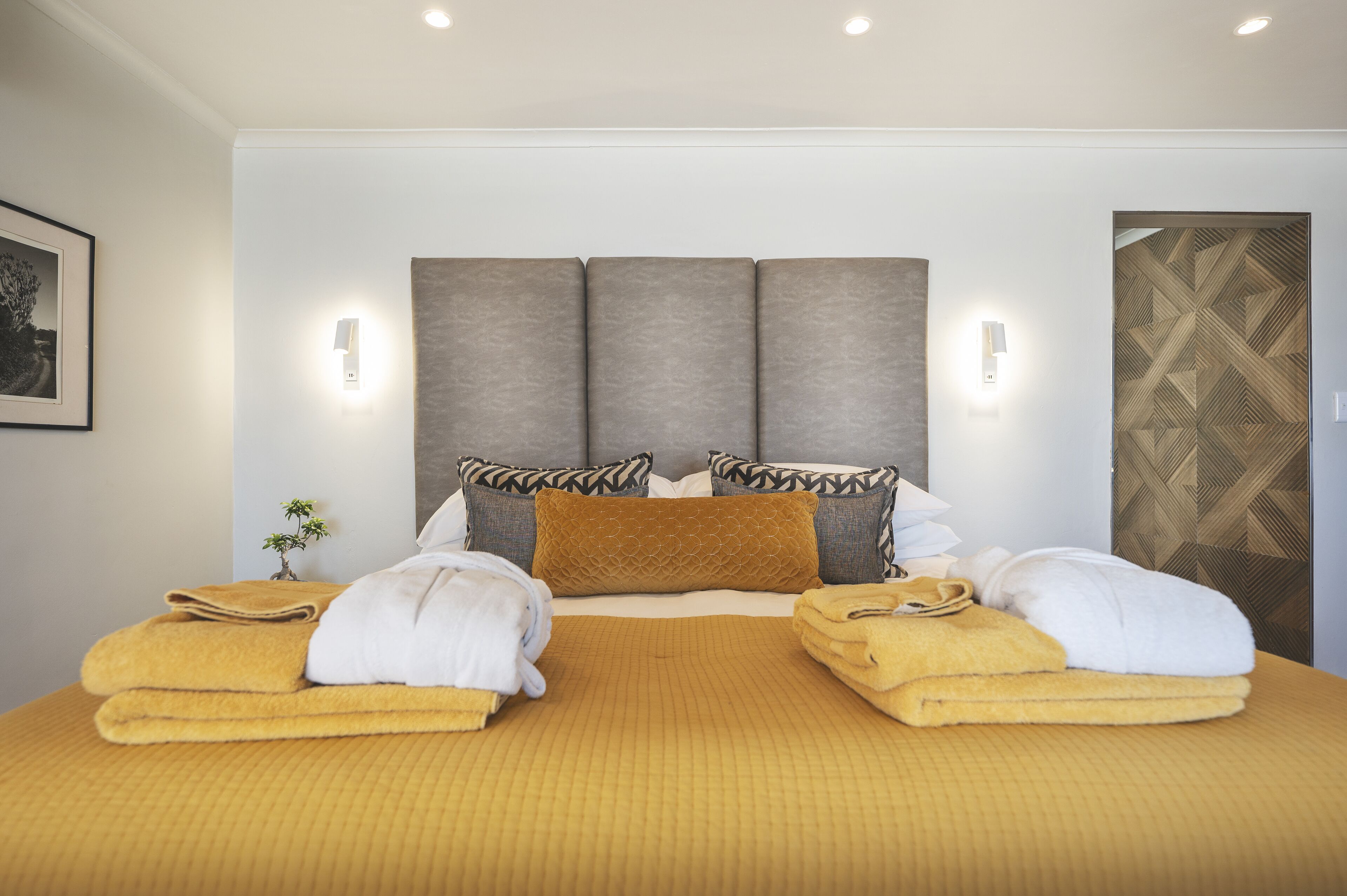 Ein ordentlich gemachtes Bett mit gelber Bettdecke, mehreren Kissen und gefalteten Handtüchern.