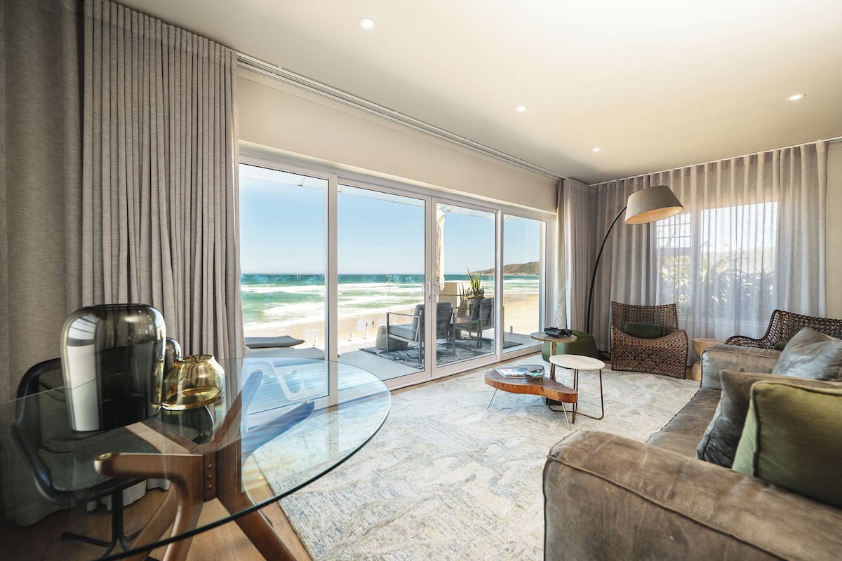 A modern living room with a glass table, a sofa, and a view of the beach.