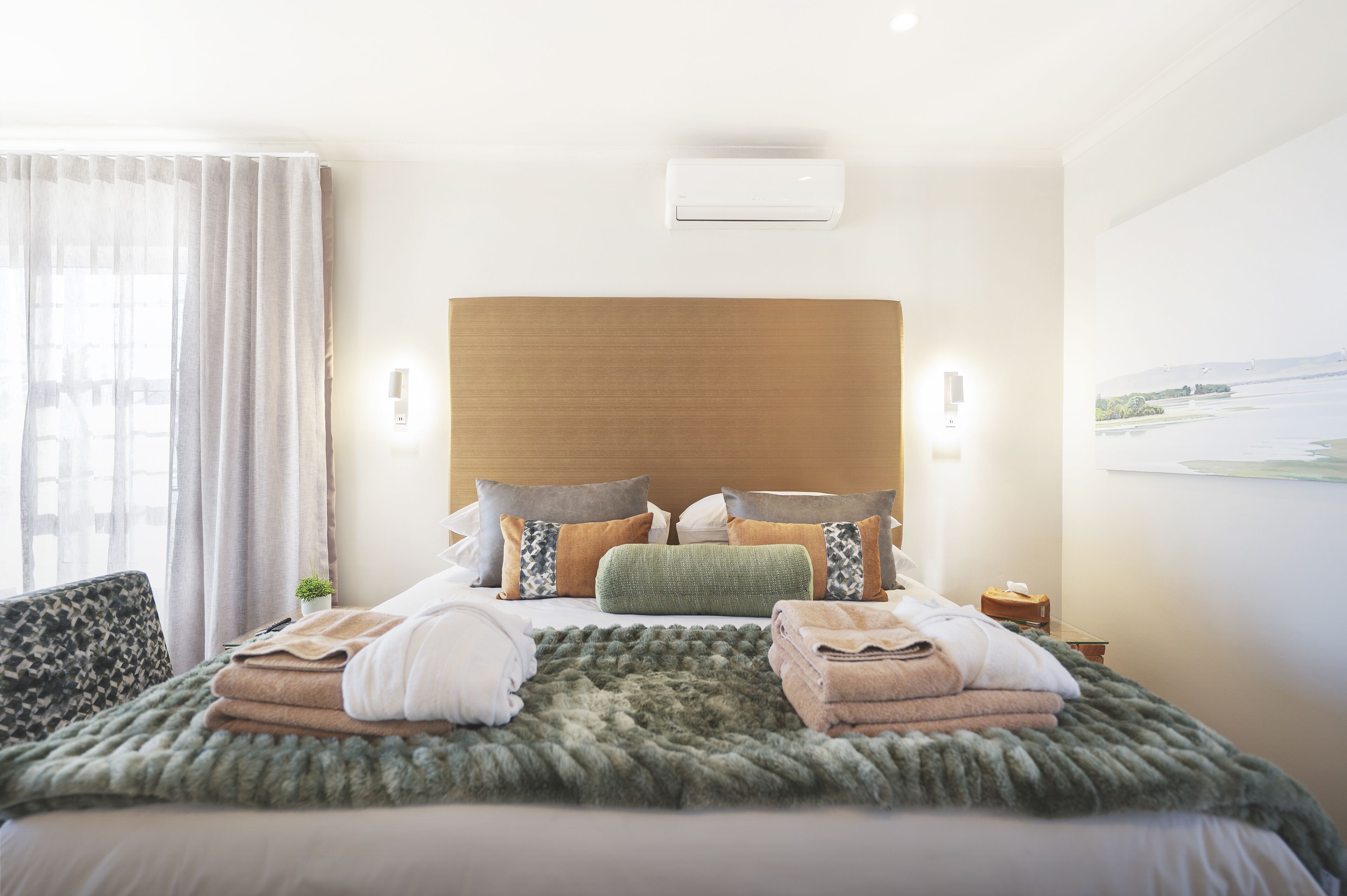 A hotel room with a large bed, a wooden headboard, a view of the sea, and a small table with a lamp.