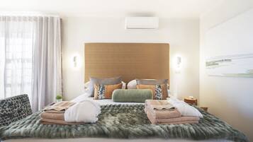 A hotel room with a large bed, a wooden headboard, a view of the sea, and a small table with a lamp.