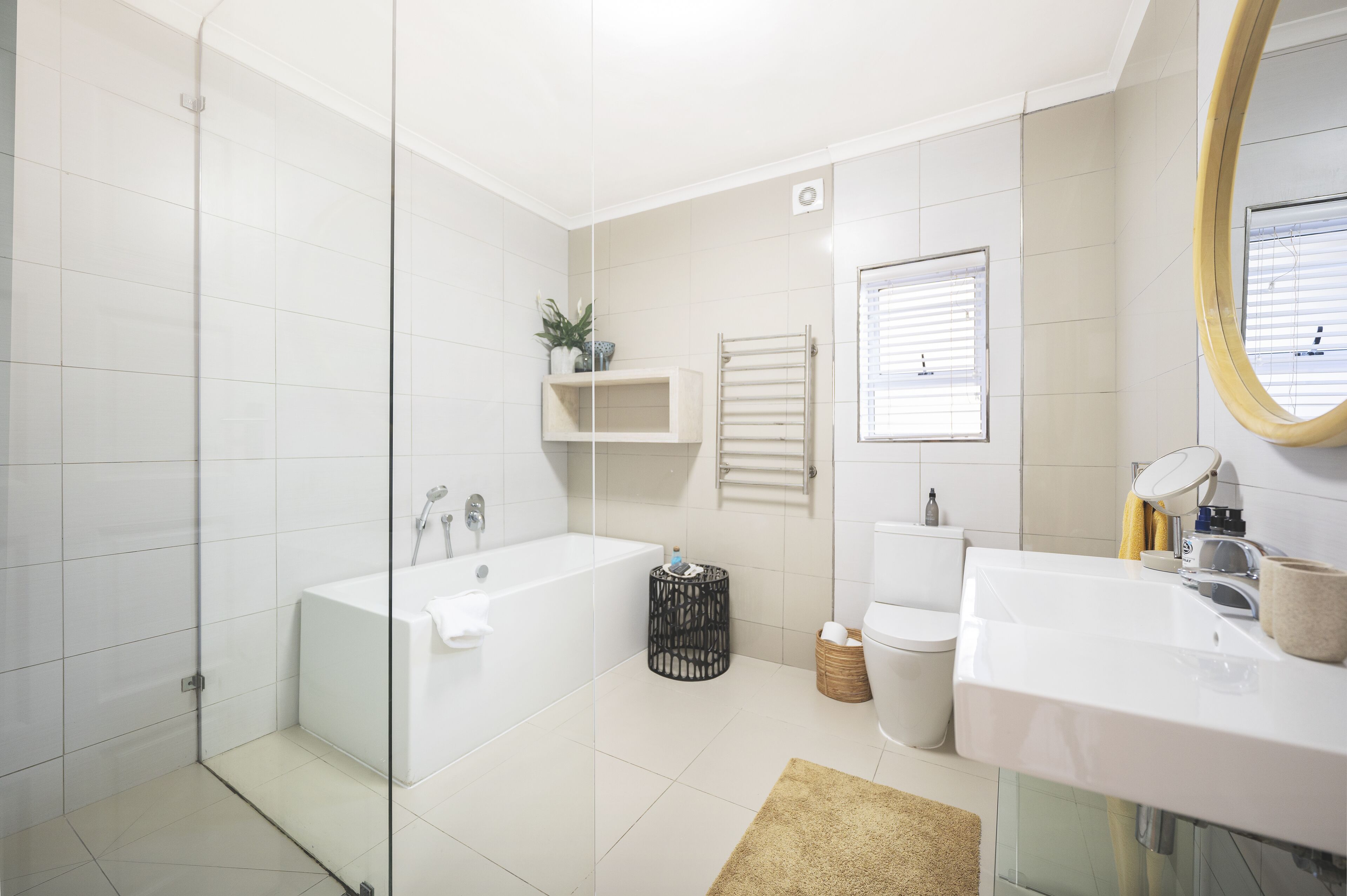 A modern bathroom with a glass-enclosed shower, a white bathtub, a sink with a mirror, and a toilet.
