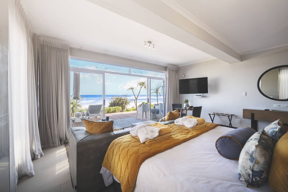 A hotel room with a large bed, a TV, a desk, and a view of the ocean.