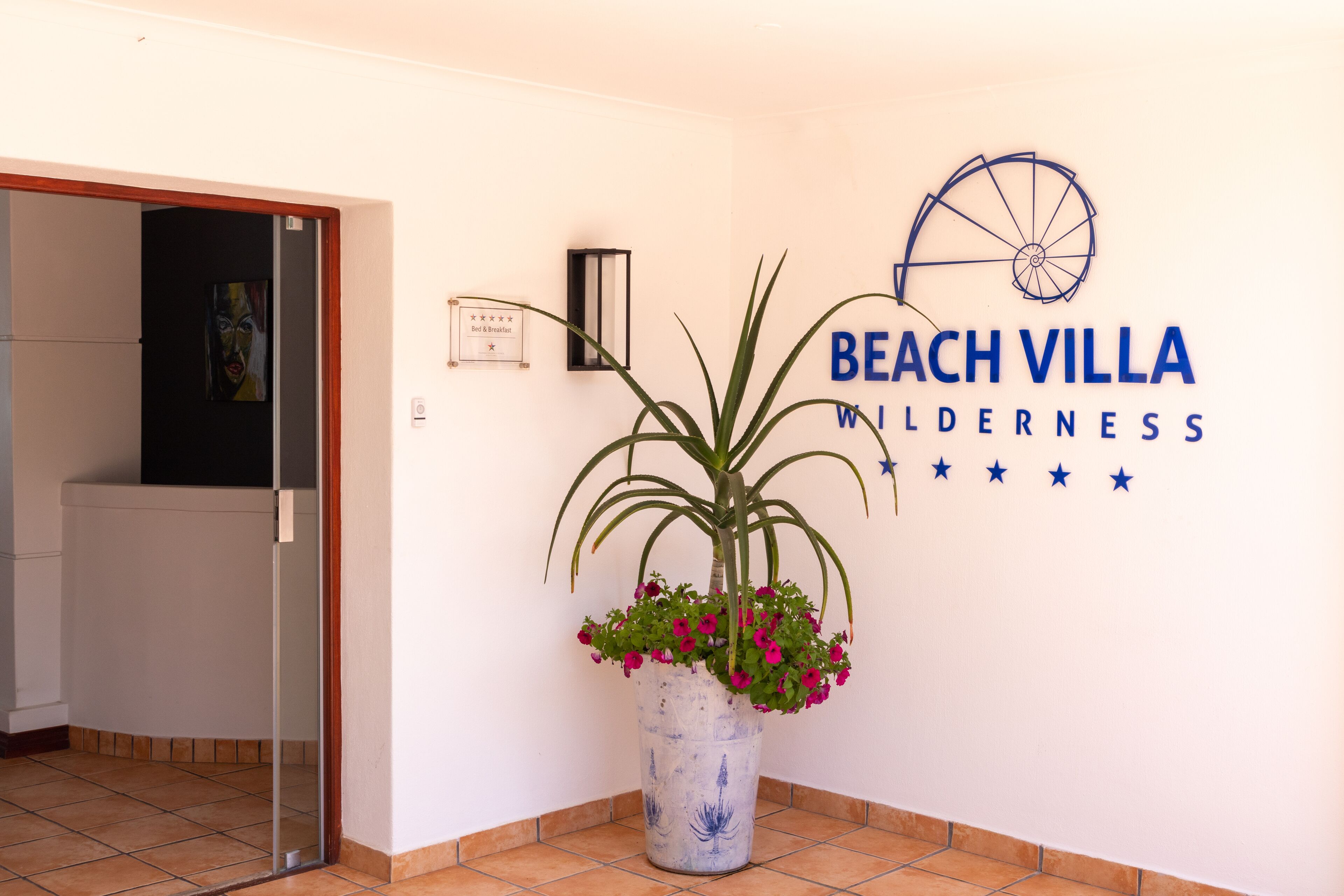 A reception area with a potted plant, a sign for 'Beach Villa Wilderness', and a bicycle wheel logo.