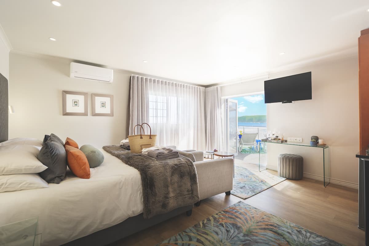 A modern hotel room with a large bed, a flat-screen TV, a balcony with a view, and a desk with a computer.