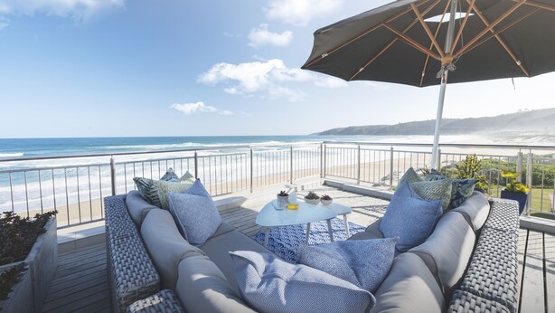 Ein Balkon mit Blick auf den Ozean, eine Couch, ein Tisch und ein Sonnenschirm.