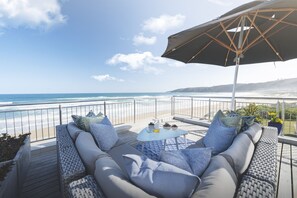 A balcony with a view of the ocean, a sofa, a table, and an umbrella. - Beach Villa Wilderness (Wilderness)