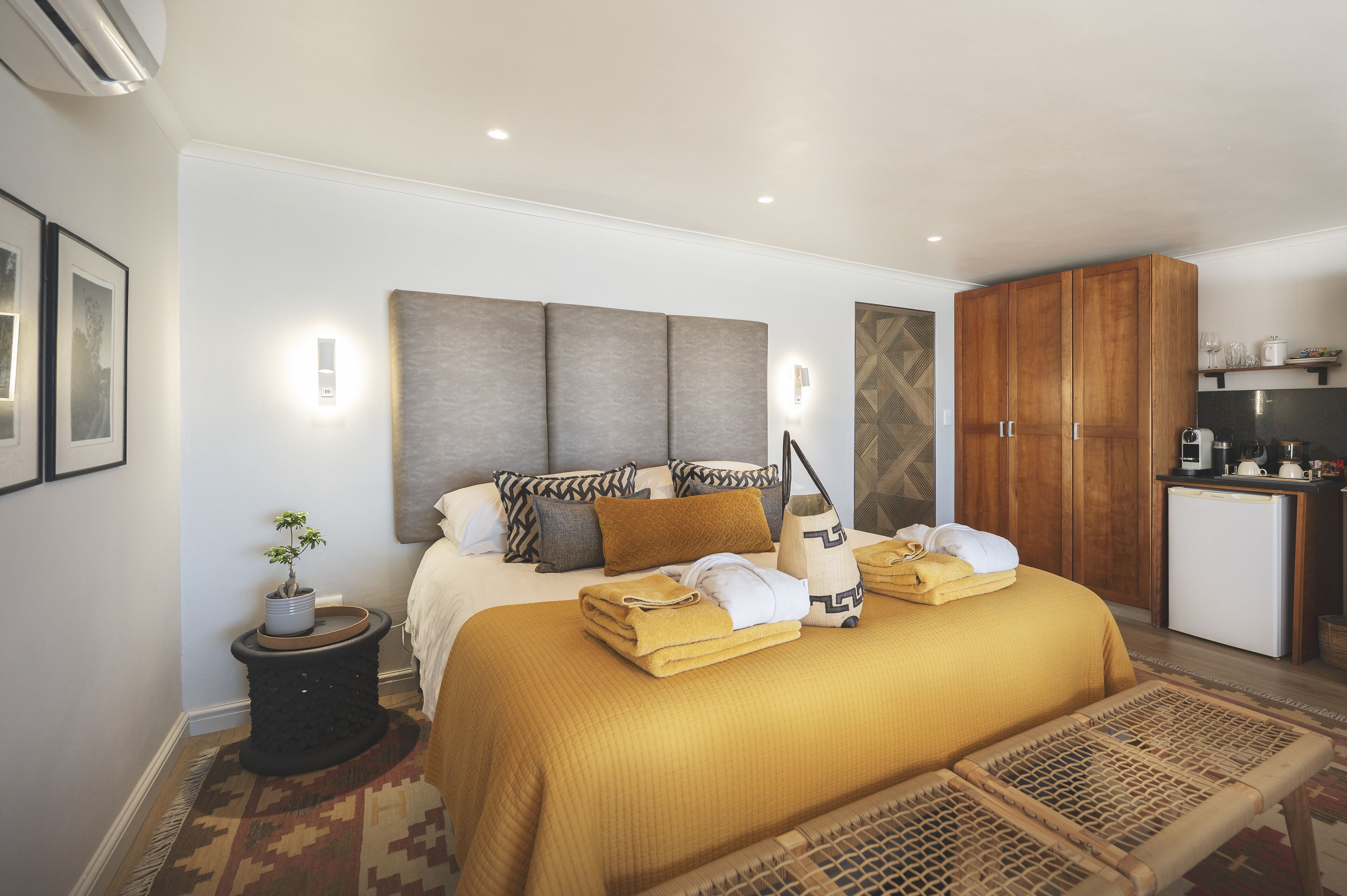 A neatly arranged bedroom with a bed, bedside table, and a small kitchenette.