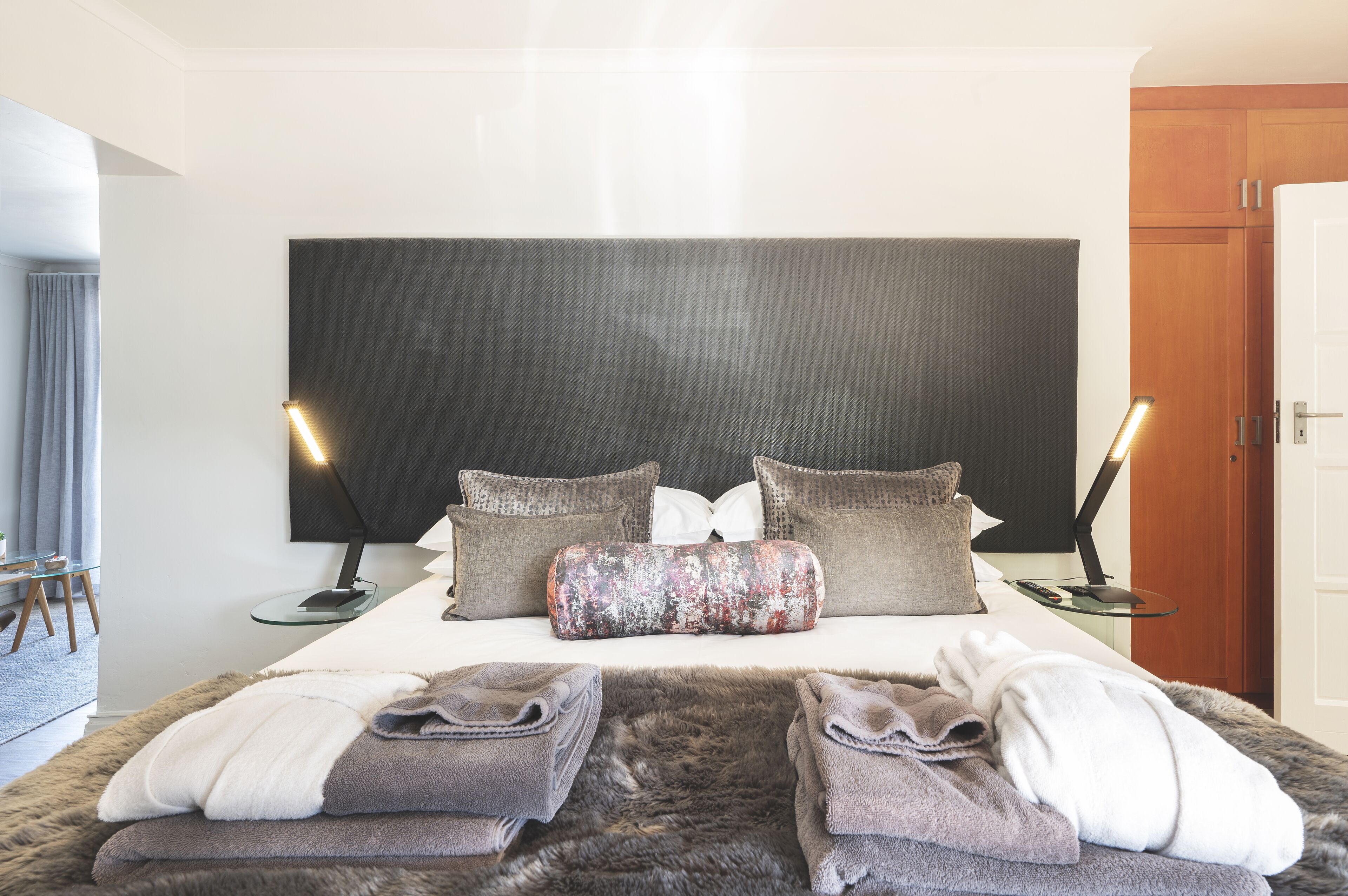 A modern hotel room with a large bed, two bedside tables, a flat-screen TV, and a wooden wardrobe.