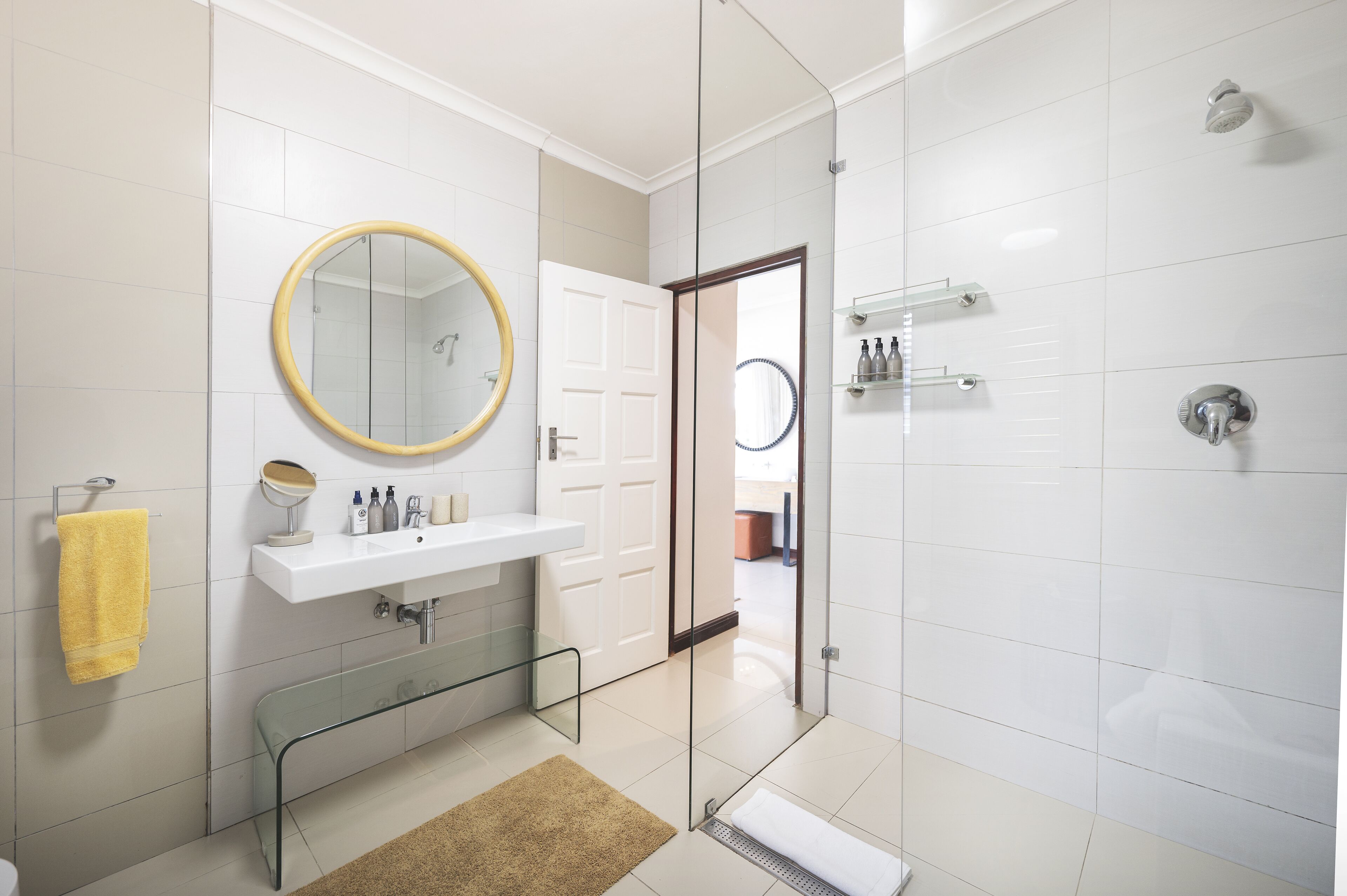 A modern bathroom with a glass shower enclosure, a white sink with a mirror, and a yellow towel.