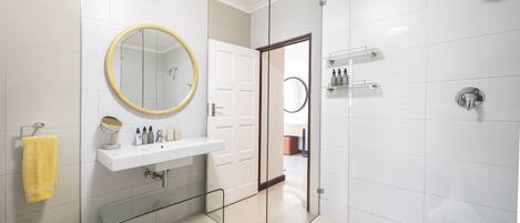 A modern bathroom with a glass shower enclosure, a white sink with a mirror, and a yellow towel.