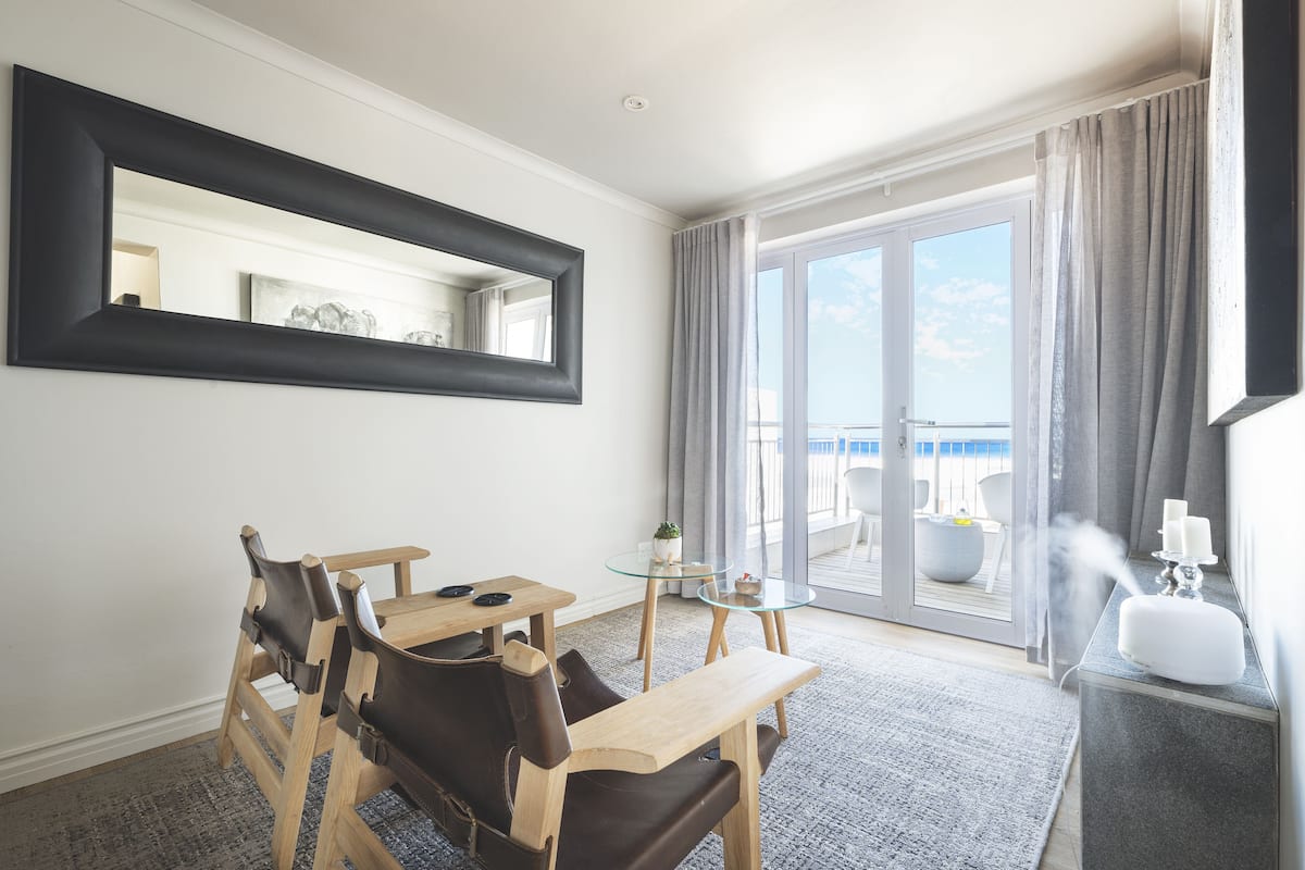 A hotel room with a dining area, a large mirror, a balcony with a view, and a modern decor style.
