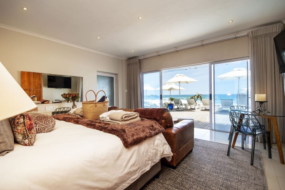 A hotel room with a large bed, a sofa, a TV, and a balcony with a view of the sea.