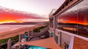 Ein modernes Gebäude mit Glasfassade und Blick auf einen Strand bei Sonnenuntergang.