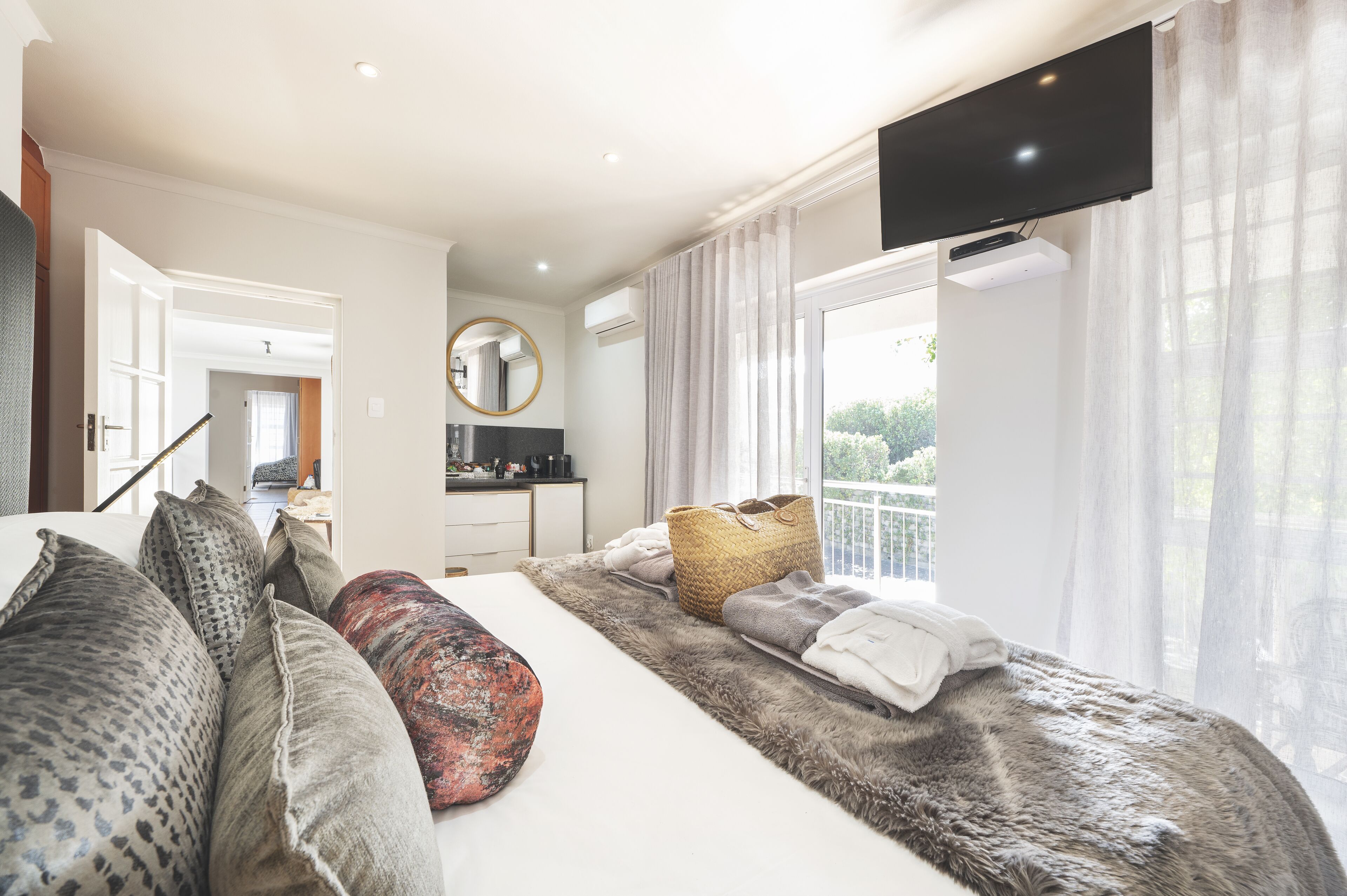 A modern bedroom with a large bed, a flat-screen TV mounted above it, and a view of the outdoors through a sliding glass door.