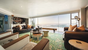 Ein modernes Wohnzimmer mit einem großen Fenster mit Meerblick, ausgestattet mit Ledersofas, einem Couchtisch und einem gemusterten Teppich.