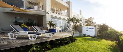 A beachfront property with a wooden deck, lounge chairs, and a sign indicating 'Beach Villa'.