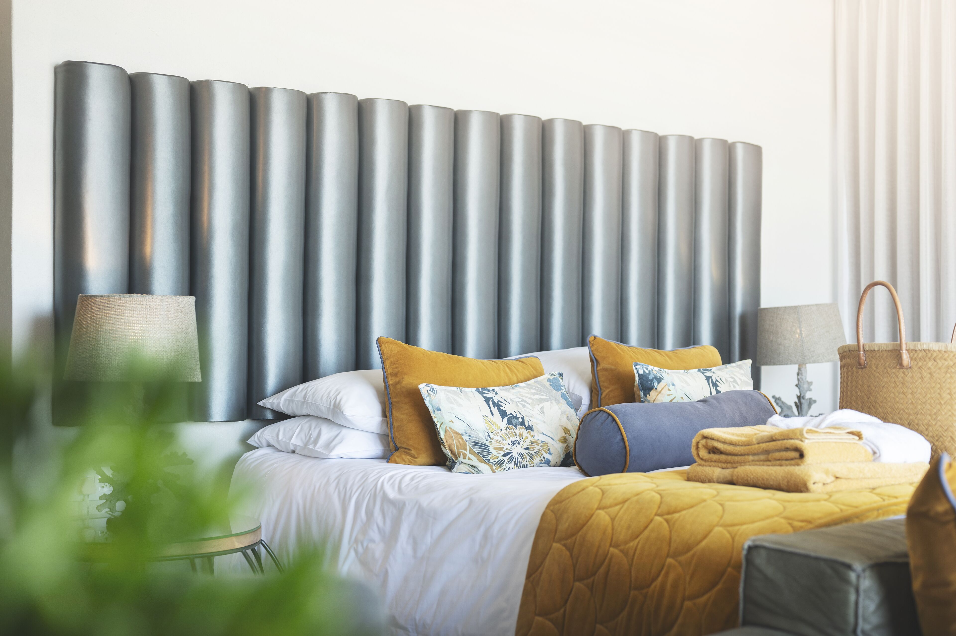 A neatly made bed with a quilted blanket, multiple pillows, and a large, cylindrical headboard.