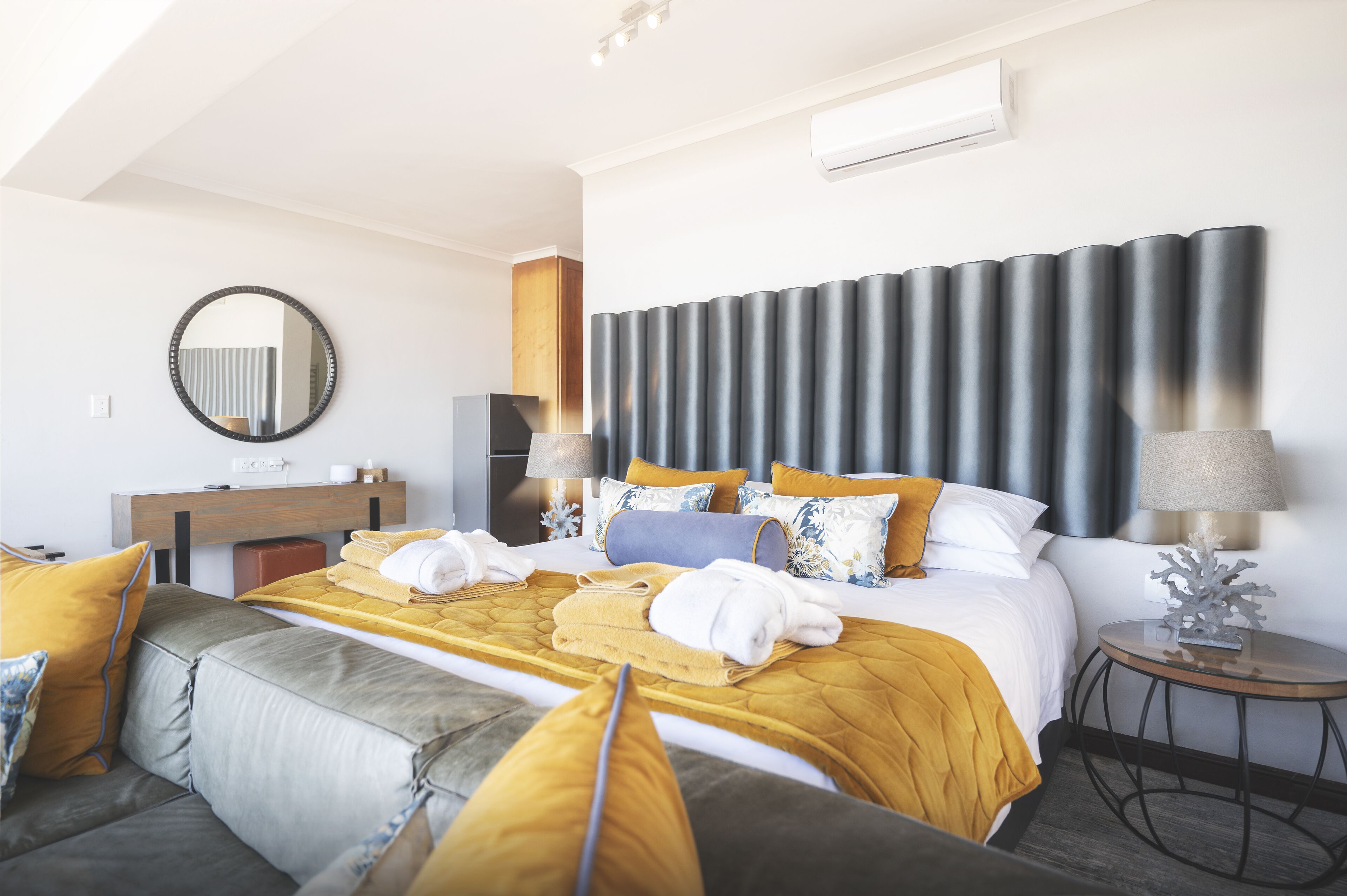 A modern hotel room with a large bed, a sofa, a round table, and a mirror on the wall.