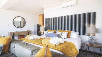A modern hotel room with a large bed, a sofa, a round table, and a mirror on the wall.
